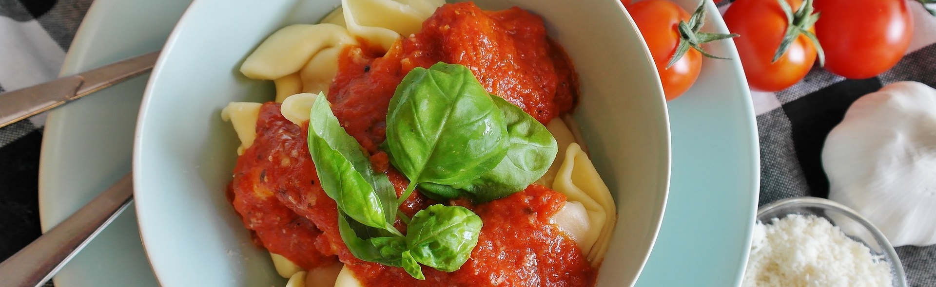 Auf einem Tablett steht ein Teller mit Tortellini und Tomaten.