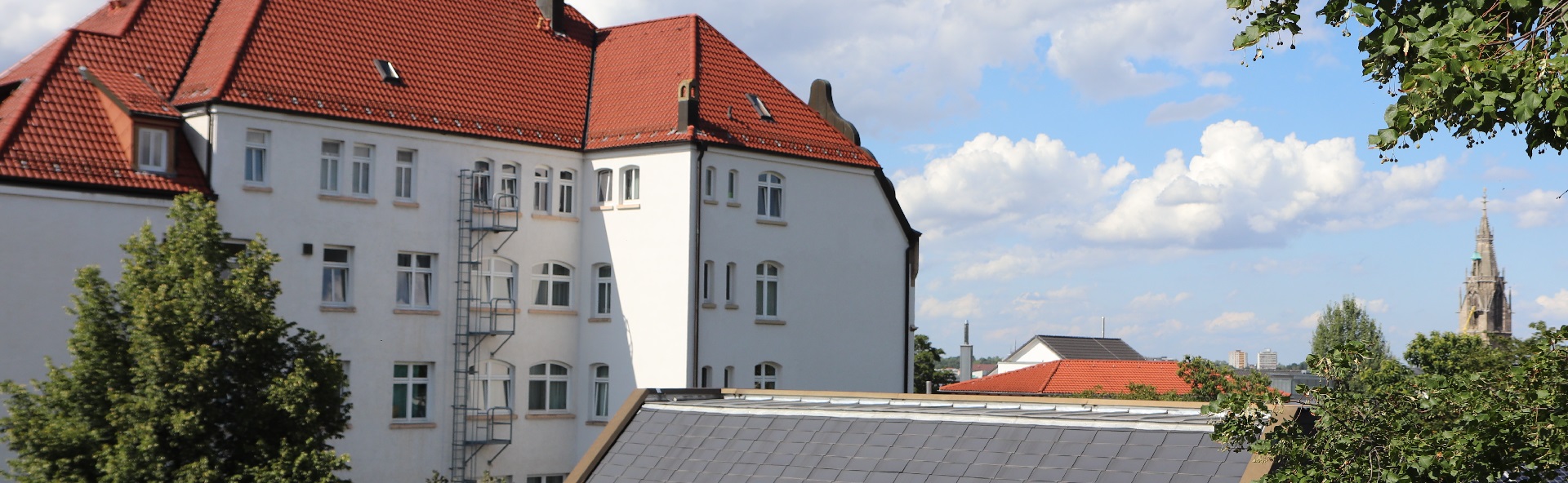Man sieht die renovierte Fassade von Haus Schempp zwischen Bäumen auf dem Campus.