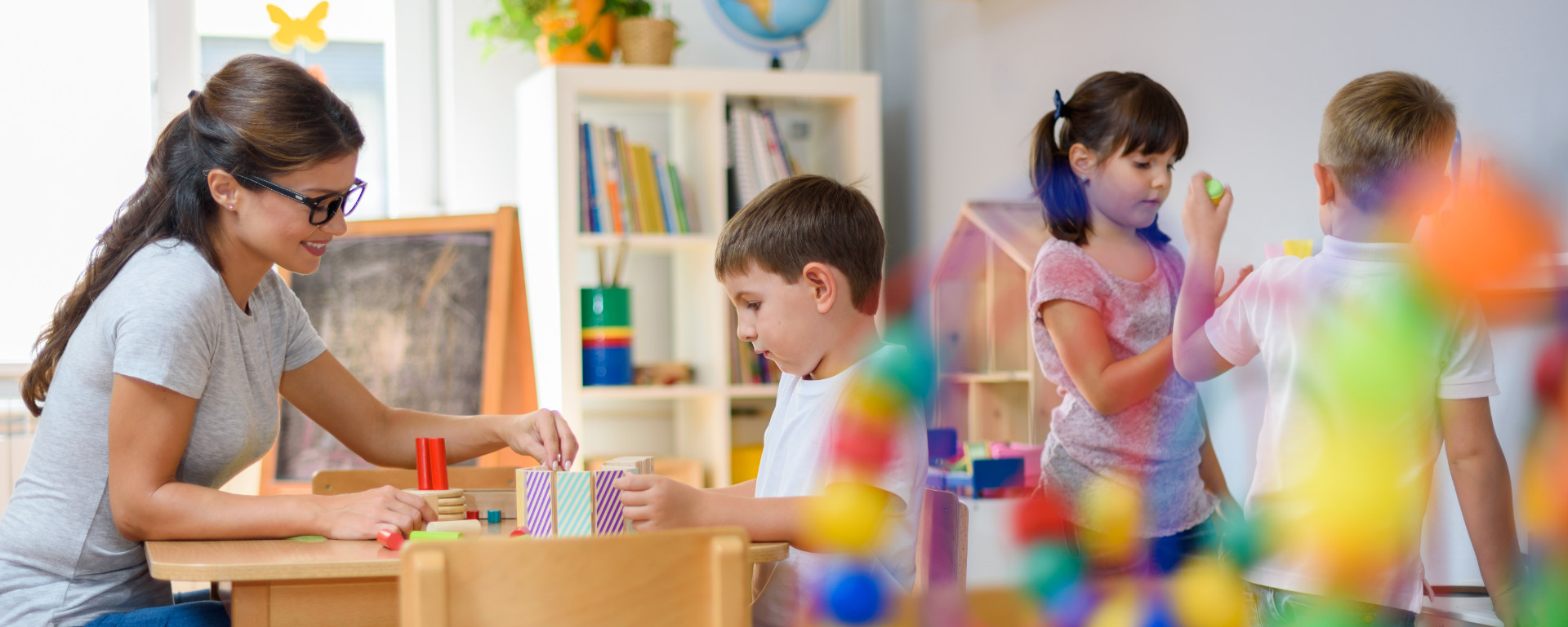 Kindergärtnerin spielt mit Kind ein Motorikspiel - Kinder spielen im Hintergrund